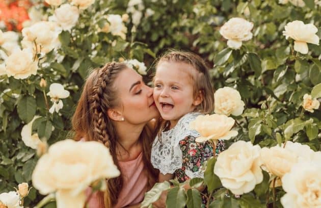 woman kissing girl's cheek between white roses garden