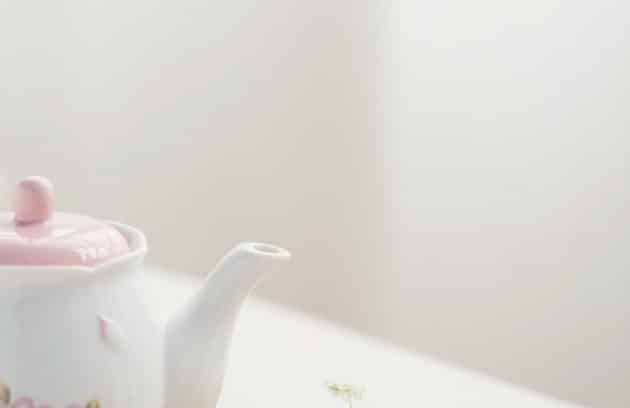 a tea pot with a pink lid sitting on top of a wooden tray