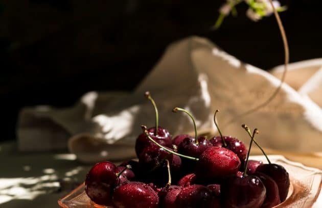 a glass bowl filled with cherries on top of a table