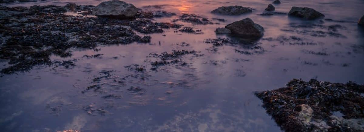 the sun is setting over the water at the beach