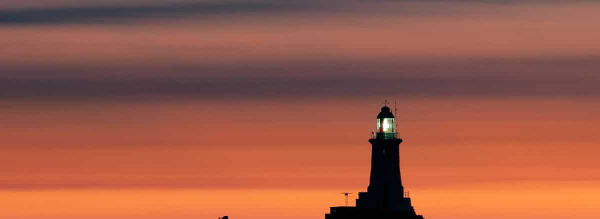 a lighthouse on a rocky outcropping at sunset