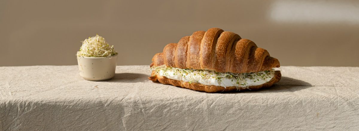 a croissant sandwich on a table next to a small bowl of cottage cheese